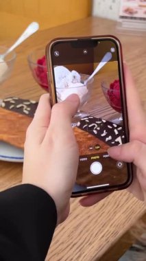 Bir kız blogger düz bir kruvasanın videosunu çekiyor, sonra onu ısırıyor, arka planda duran iki porsiyon dondurmayı tadıyor, kiraz ve vanilya. Tatlı lezzetli.