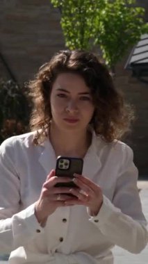 Telefonu olan bir kız, Smartphone 'u bir arkadaşına götürmek için caddede yürüyor. Telefonla acele etmek için internet bağlantısı kuruyor. Kıvırcık saçlı beyaz gömlek