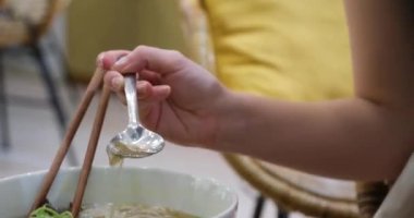 Restoranda pho bo çorbası servis ediyorum. Kadın turist sokak pazarında keyif çatar ve Tayland pilavlı erişteyi kasede ve sokak yemeklerinde tek başına karıştırır ve yer. Vietnam 'da fo çorbası içiyorum.
