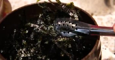 Açık mavi arka planda beyaz bir kasede doğranmış nori yaprakları. Chia tohumlarından vegan havyarı pişirme basamağı.