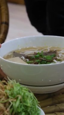 Restoranda pho bo çorbası servis ediyorum. Kadın turist sokak pazarında keyif çatar ve Tayland pilavlı erişteyi kasede ve sokak yemeklerinde tek başına karıştırır ve yer. Vietnam 'da fo çorbası içiyorum.