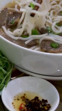 Restoranda pho bo çorbası servis ediyorum. Kadın turist sokak pazarında keyif çatar ve Tayland pilavlı erişteyi kasede ve sokak yemeklerinde tek başına karıştırır ve yer. Vietnam 'da fo çorbası içiyorum.