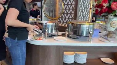 Suşi büfesinden lezzetli yiyeceklerle dolu beyaz bir tabak. Somon nigiri ve maki rulo. Bir el maki dürümlerinden birini yemek çubuğuyla alıyor. Ho Chi Minh Şehri Vietnam 06.06.2024