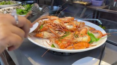 Suşi büfesinden lezzetli yiyeceklerle dolu beyaz bir tabak. Somon nigiri ve maki rulo. Bir el maki dürümlerinden birini yemek çubuğuyla alıyor. Suşi büfesi. Yemek Konsepti. Haşlanmış karides