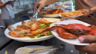 İki kişinin elleri yengeç ve karides topluyor. Tabak açık büfede. Karides yengeci tabağı