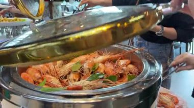 Suşi büfesinden lezzetli yiyeceklerle dolu beyaz bir tabak. Somon nigiri ve maki rulo. Bir el maki dürümlerinden birini yemek çubuğuyla alıyor. Suşi büfesi. Yemek Konsepti. Haşlanmış karides