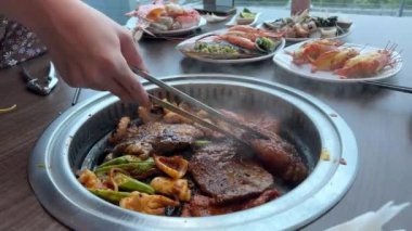 Izgarayı Kore restoranında et pişirmeye hazırlarken garson su ekliyor. Biftek pişirmek. Restoranda barbekü. Masada kızarmış et.