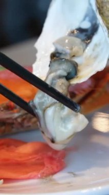 Bir midyeyi kabuğundan çıkarır, açık deniz ürünleri restoranında yemeden önce taze limon suyu sıkar. Yemek çubuklarıyla istiridye ayıkla.