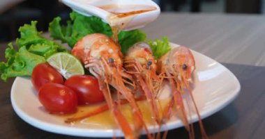 Profesyonel şef akşam yemeği için lezzetli bir tabakta karideslerin üzerine yeşil sos döküyor. Haşlanmış karidesin üzerine balık sosu serpiştir. Karidesin üzerine sos dök.