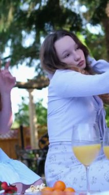 İki kız arkadaş piknikte portakal suyu içerek selfie çekerek telefonlarının başında oturup yaz elbiseleriyle çimde oturarak konuşuyorlar. İki arkadaş pikniği