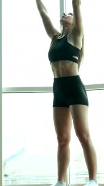 Spor salonundaki kadın esniyor. Genç bir kadın esneme egzersizleri yapıyor. Spor yapan genç bir kadın oturma odasında tek başına egzersiz yapıyor. Sağlıklı vücut yaşam tarzı konsepti için evde egzersiz.