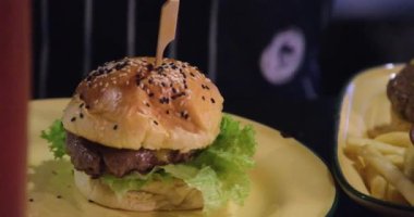 İçinde salata ve köfte olan klasik bir hamburger ekmeğini sıkıyorum. Damlayan çizburger sosu. Tahtadaki makro.