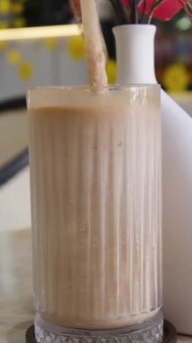 Krema dökülmüş uzun bir bardakta buzlu kahve. Koyu beton bir masada buz küpleri ve fasulyeler. Hindistan cevizi ve kremalı buzlu latte.