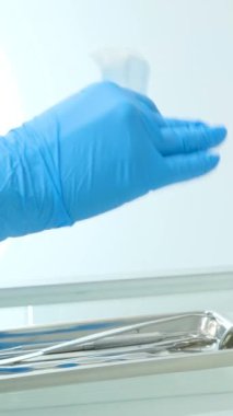 Cerrahi eldivenlerini çıkarıp ameliyat odasında giyerken, erkek veteriner ellerini yakınlaştırın. Arka planda beyaz duvarlar ve kapı var. Dişçi araçları açılıyor