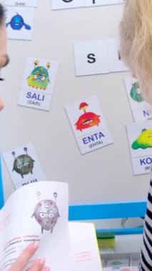 Okul sınıfındaki bir grup ilköğretim öğrencisine hikaye okuyan bayan öğretmen. Genç öğretmen ve anaokulu öğrencileri bir anaokulunda sınıf öğretmenine oturuyor ve bir kıza mektup okumayı öğretiyor.
