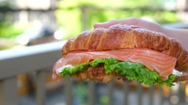 Bir kız, somon ve süzme peynirle doldurulmuş taze bir kruvasanı bir kafede yer. Kırmızı balıklı kruvasan