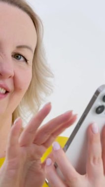 Telefondaki haberlere göz gezdirirken, beyaz arka plandaki parlak elbiseli yetişkin bir kadın, haberlere, sosyal ağlara bakıyor, reklam arıyor, satış, mesaj için yer arıyor, sarışın.