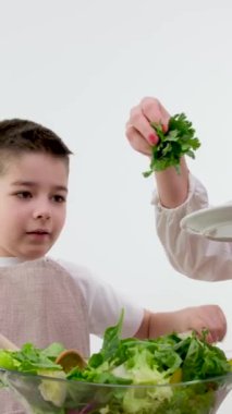 Anne ve oğlunun mutfakta birlikte yemek pişirmesini yakın çekim, mutlu çocuk annesine yemekte ya da öğle yemeğinde yardım ediyor, marul yapraklarını cam bir kaseye döküyor. Yüksek kalite