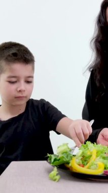 Aile mutfağında yemek yapıyor. Son, annesine nasıl sebze yeneceğini öğrenmek için salata veriyor. Aile ilişkisi. Çocuk salata yemeyi öğreniyor.