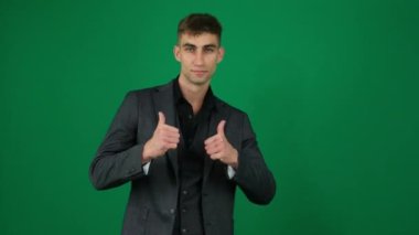 Yeşil arka plandaki yakışıklı adamın duyguları... Kromakey yakın plan koyu renk saçlı genç adam... iş ilanı. Parmak 'ın iki elini de uzaya kaldırmasını onaylayın. bir ürün öneriyor
