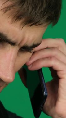 Mans, yeşil arka plandaki yakışıklı bir adamın telefon konuşmalarıyla yüzleşiyor. Koyu renk saçlı genç adam. Elle konuşma, SMS çevrimiçi arama cihazı patronluk işi. reklamcılık