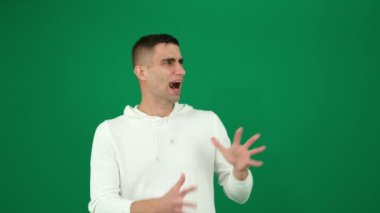 Yeşil arka plandaki yakışıklı bir adamın duyguları. Koyu renk, yakın plan, genç adam. Şok, sürpriz, korku, insan parmaklarını uzatarak oturur, korku içinde saklanır, ağzı açık bakar.