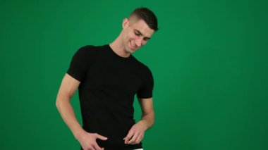 Seksi adam tişörtünü kaldırıyor. Yeşil arka plan krom renkli, yakın plan koyu saçlı yakışıklı bir adamın duyguları. Genç adam. Spor kulübünde güzel bir gövde gösterisi.