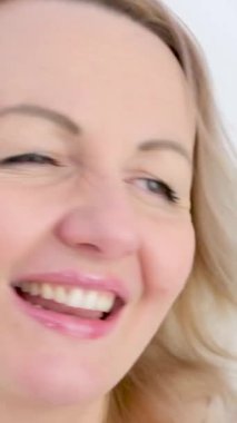 Sarışın bir kadın el sallıyor, başını sağa sola çeviriyor, gülüyor, dans ediyor, omuzlarını silkip beyaz arka planda, gözleri seksi yapıyor. 