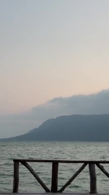 Dağlar sisin içinde denizin arka planına karşı görünür. Küçük tahta köprü