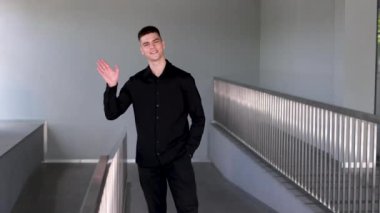 Adam el sallıyor. Siyah saçlı ve mavi gözlü yakışıklı bir adam. Melez ırk uyruğu. Orta Doğulu bir adam kameranın önünde milleti selamlıyor, el sallıyor ve gri arka planda gülümsüyor.. 