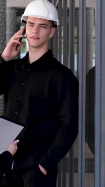 Kasklı genç erkek ve kadın inşaat mühendisleri inşaat halindeki bir binanın üzerinde ellerinde oyuncak tablet telefon inşaatı tutuyorlar. Birlikte çalışıyoruz.