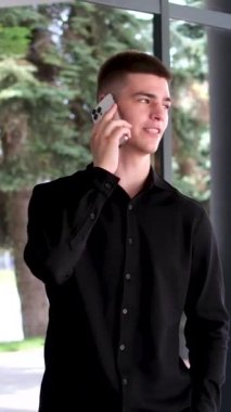 Modern iş yeri binasının yakınında gündelik yürüyen yakışıklı, mutlu sakallı iş adamı akıllı telefonu elinde tut. Yetişkin Erkek Girişimci Seo Yöneticisi yaşam tarzı dışında bir cep telefonu oku