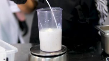 Mutfakta cam bir kasede bir kadın sütle tereyağını çırpıcıyla karıştırıyor. Tarife göre hamur işi pişirirken tereyağlı süt çırpmak. Tarife göre süt dök.