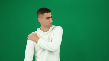 Omuz ağrısı geçti. Yeşil arka plandaki yakışıklı bir adamın duyguları. Koyu renk, yakın plan, genç adam.