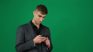 Adam telefonda mesaj yazıyor. Yeşil arka plandaki yakışıklı adamın duyguları... Kromakey yakın plan koyu renk saçlı genç adam. Elden konuşma, SMS 'i ara, internetten arama cihazı, patron. iş reklamcılığı