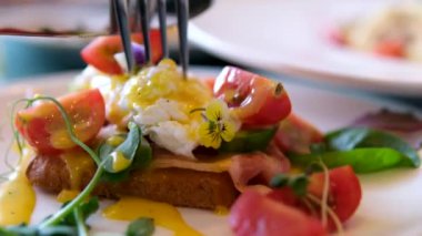 Benedict yumurtasını kes. Sağlıklı sabah yemeği. Otelde kahvaltıda nefis haşlanmış yumurta yiyen bir adam. Erkek eli Benedict yumurtasının içini yumurta sarısı, hollandez sosu ve ıspanak ile keser.