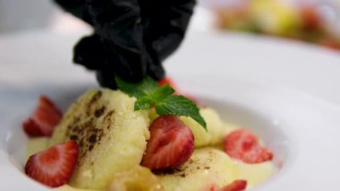 Çilekli bir turtanın üstüne çilek dilimi yerleştiren siyah eldivenli bir şefin elini yakın plan. Pastayı süsle. Çilek yapma süreci. Peynirli tatlı. 