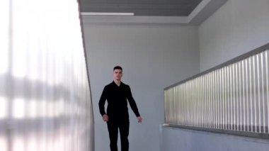Genç işadamı uzun ofis koridoru boyunca gidiyor. Kamera arkası pencereli. Takım elbiseli bir adam işe gitmek için salonda yürüyor. Ofis stili oluşturma başarılı