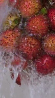 Suyun altında meyve yıka. Paslanmaz kasede seçici yumuşak odaklı rambutan lavabodaki musluktan taşan suyla yıkanmış tüketimi artırmak için su tasarrufu yapmamış. Su hareket halinde akıyor.. 