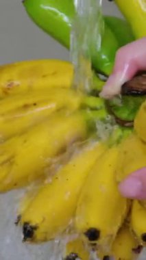 Suyun altında meyve yıka. Paslanmaz çelik bir lavaboda akan bir avuç olgun muz, besin güvenliği ve hazırlığı betimliyor.