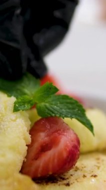 Çilekli bir turtanın üstüne çilek dilimi yerleştiren siyah eldivenli bir şefin elini yakın plan. Pastayı süsle. Çilek yapma süreci. Peynirli tatlı. 