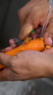 Mutfak lavabosunda havuç yıkayan, akan suyun altında suyu silkeleyen bir kadının yakın çekim, yavaş çekimi. Akan suyun altında havuç soy.