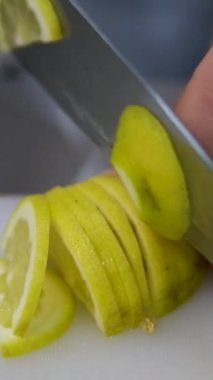 Limonu dilimlere ayır. Limon, keskin bir mutfak bıçağıyla plastik bir kesme tahtasıyla kesilir.