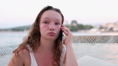 Telefondaki kadının tatminsiz konuşması teslimat sipariş etmesi, arkadaşlarıyla iletişim kurması, sosyal ağlar ve internet kullanması. Yanık tenli genç bir kızın plaj duygularında dinleniyor. kırmızı yanaklar ıslak saçlar.
