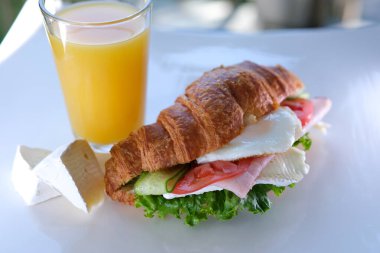 Etli kruvasan. Kahvaltı yemeğinin yakından görüntüsü: pastırmalı kruvasan sandviç ve çırpılmış yumurta. Sabahları Bali kafeteryasında servis edilen etli orjinal lezzetli yemek.