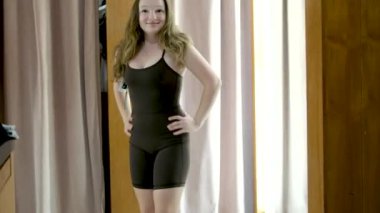 Moda kızı aynaya bakar ve alışveriş merkezinin mağazasındaki kıyafetleri dener. Alışveriş merkezinde aynada poz veren mutlu kız. Kız müşteri turuncu spor giysiler alıyor.