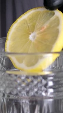 Cama limon ekle. Limonata yapmak, yaz içkisi, soğuk içecek, sağlıklı sıvı. Bir bardağa bir dilim limon at kadın elinin limon dilimini kapat içine su ve mavi bardakta buz koy. 