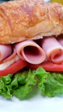 Etli kruvasan. Kahvaltı yemeğinin yakından görüntüsü: pastırmalı kruvasan sandviç ve çırpılmış yumurta. Sabahları Bali kafeteryasında servis edilen etli orjinal lezzetli yemek.