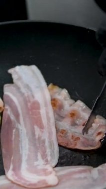 Tava manzaralı domuz pastırması yavaş çekimde yakın çekim. Kızarmış aromalı pastırma dilimleri daha iyi pişirmek için tavaya konur. Güne geleneksel kahvaltıyla başla. Kızarmış domuz