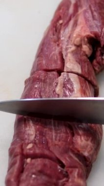 Şef mutfak masasının önünde bıçağını biliyor. Aşçı çiğ et ve çeşitli sebze filetosu kesmeden önce aletlerini hazırlıyor. Çiğ biftek kesimi.